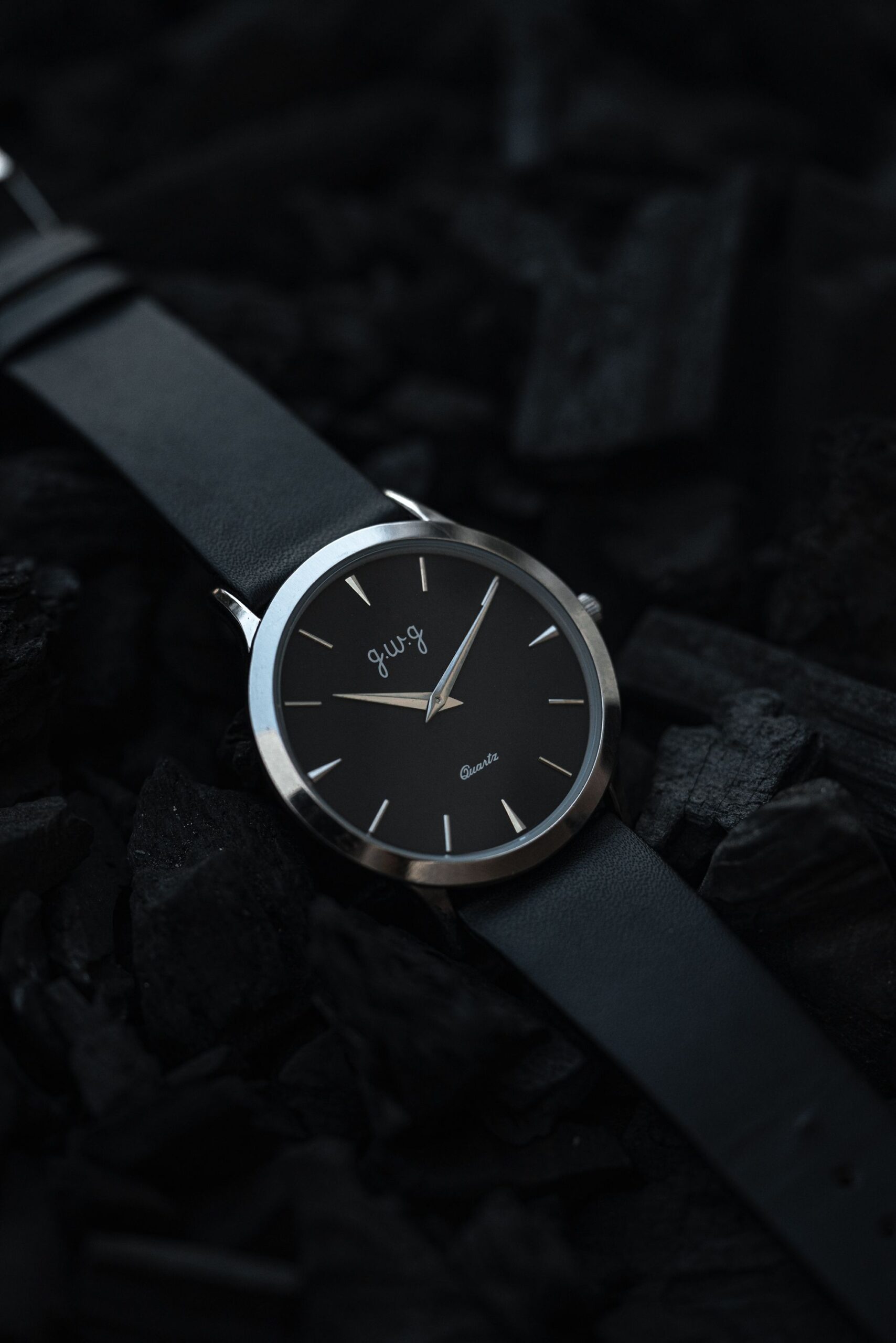Black minimalist wristwatch with a leather strap displayed on a dark textured background.